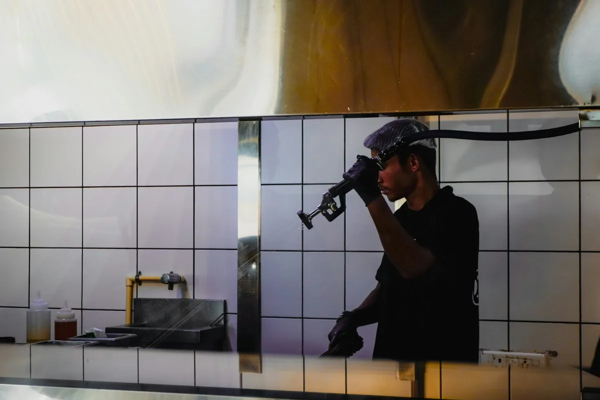 Man in black shirt and hard hat using a tool. — professional food preparation environment
