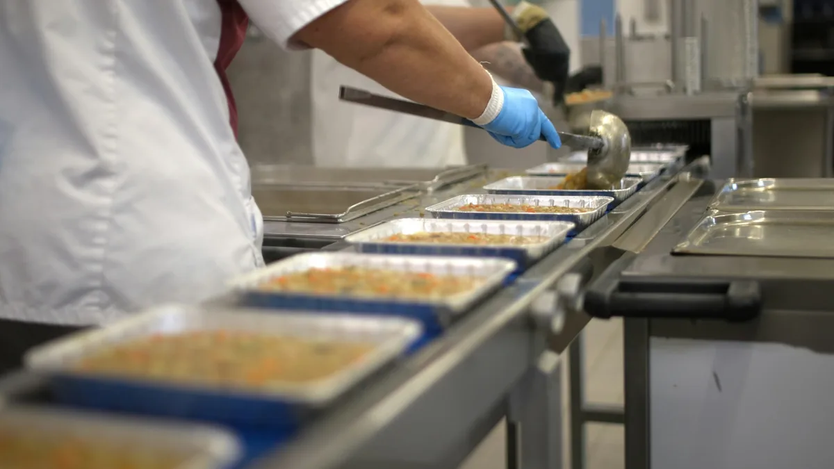 Worker filling food trays on a conveyor belt. — professional food preparation environment