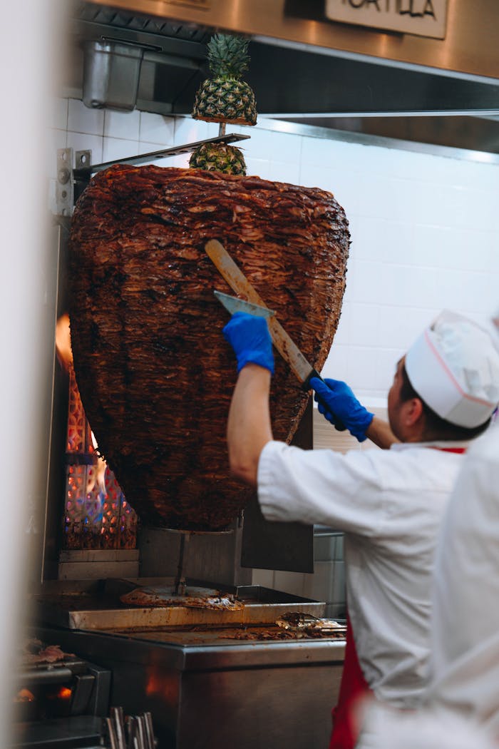 A chef expertly slices a large al pastor shawarma in a New York City kitchen.