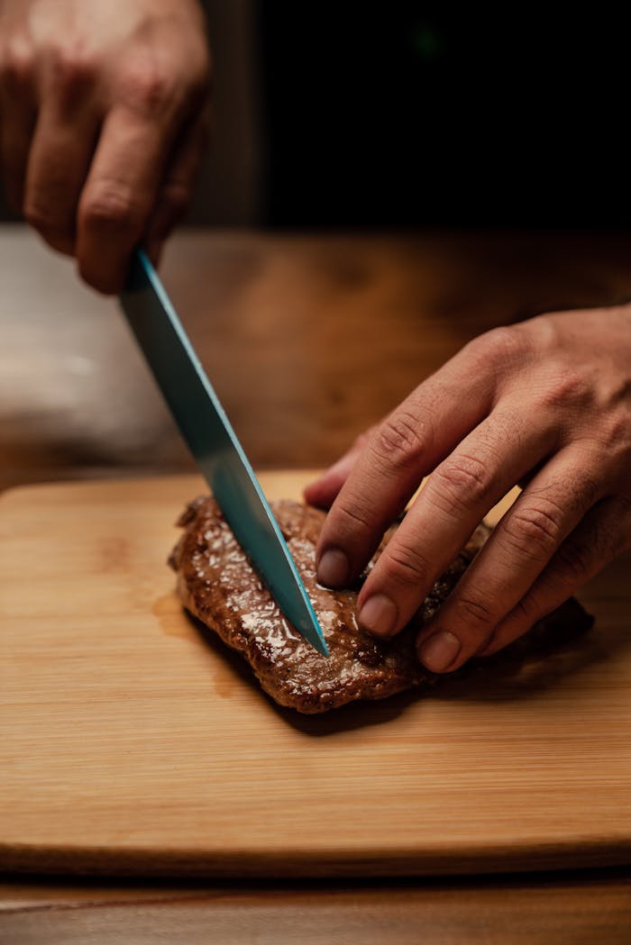 services-02 Close-up of hands slicing a juicy steak on a wooden cutting board, showcasing food preparation.