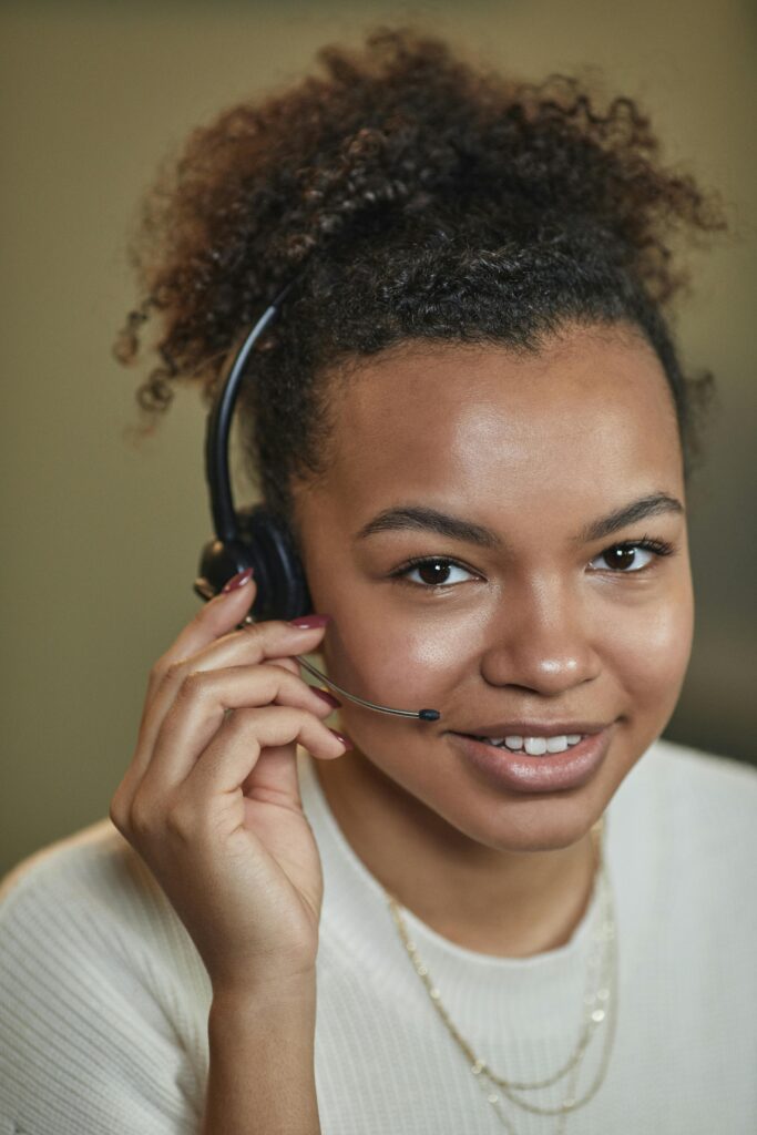 pexels photo 7689659 7689659 Close-up of a smiling woman with afro hair wearing a headset, providing customer support.